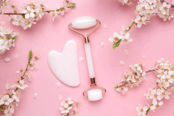 istock Gua sha stone, face roller for face massage on a pink background with blooming cherry. Cosmetic facial skin care and spa. Natural treatment concept 1392905893