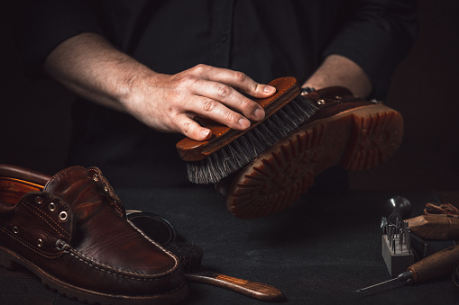 A shoemaker cleans boots with a brush in his workshop. Shoe Shine