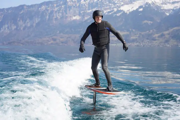 He surfs the wake behind boat in Lake Thun, Swiss Alps behind