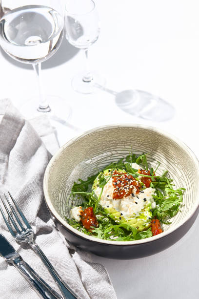 istock Avocado and stracciatella cheese salad. Fancy dinning with Italian salad bowl on white table with simple contemporary decor. Sunlight and harsh shadow still life. Avocado, cheese and tomato salad. 1392909979