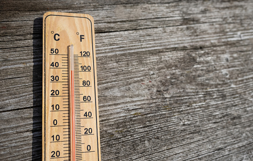 Wooden thermometer with red measuring liquid showing high temperature over 32 degrees Celsius on sunny day on old wooden background. Concept of heat wave, warm weather, global warming, climate change