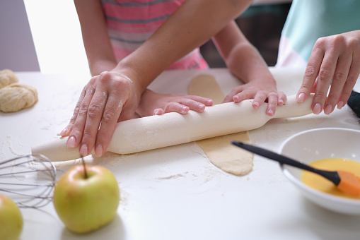 Mom and daughter roll out the dough with rolling pin in kitchen. Family cooking pastry concept