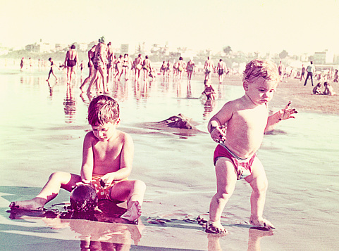 Vintage image of a baby girl and a young boy playing with the sand at the beach. Vintage image from the seventies.