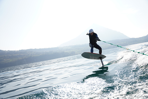 Holding on to rope, he surfs the wake behind boat in Lake Thun, Swiss Alps behind