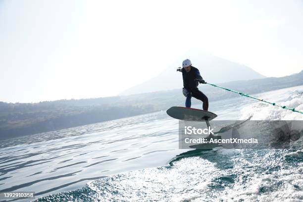 View Of Man Riding Wake Foil Behind Motor Boat Stock Photo - Download Image Now - Aquatic Sport, Rope, Wakeboarding