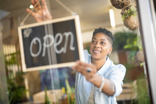 LGBTQ+ woman hanging open sign in store window LGBTQ+ female small business owner working in florist using technology open sign stock pictures, royalty-free photos & images