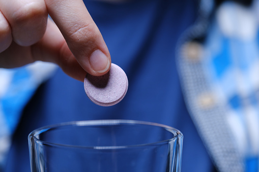 Human hands are dissolving an effervescent tablet in a glass of water