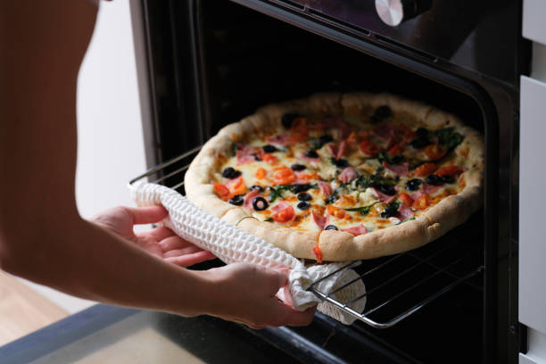 istock Woman puts pizza pan in oven closeup 1392912150