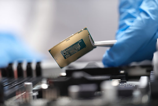 Engineer is holding microprocessor tweezers from motherboard. Microchip testing concept