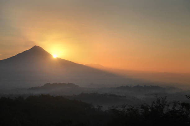 This picture was taken in Punthuk Setumbu, a hill visited by many people to see the sunrise, you may see the Mount Merapi and the rays of light behind it, the sun were ready to arise, combine with cloudy/ foggy wheather in the morning, at the right side of the picture you may see the silhouette of Borobudur temple, a buddhist temple in Indonesia that gained worldwide fame.