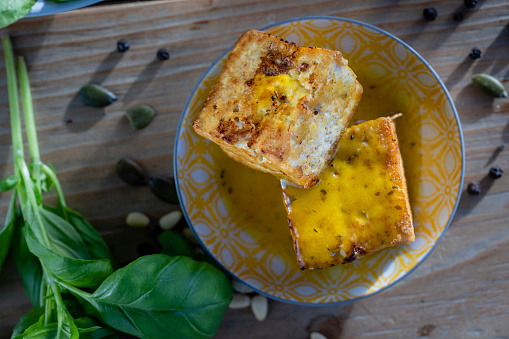 A close-up shot of a healthy bowl of fried tofu on a rustic wooden table with spinach, pumpkin seeds, and pine nuts surrounding.