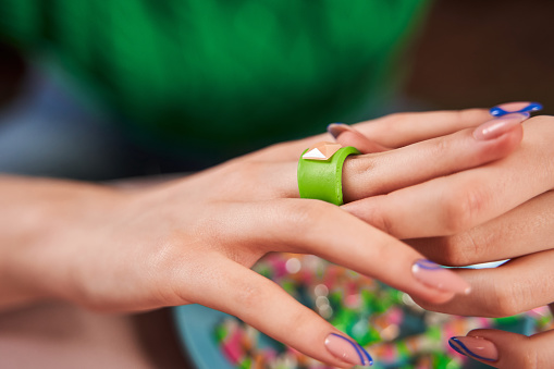 Cropped view of the teen girl with fresh manicure trying on her new hand made ring while spending time at home. Stock photo