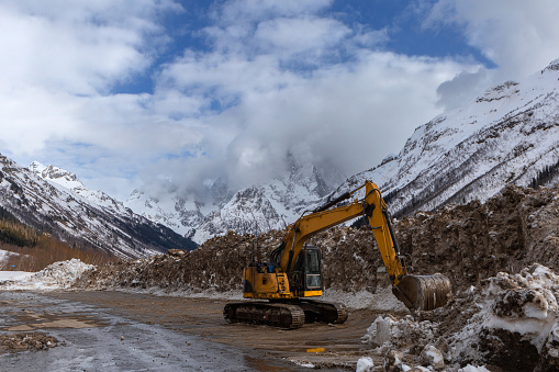 An excavator clears snow against the backdrop of the high, snow-covered Chotcha Mountain in Karachaevo-Cherkessia.