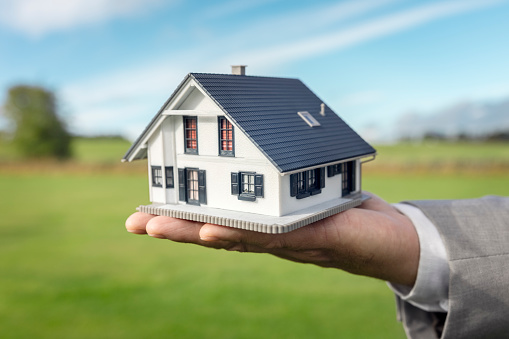 Holding a model detatched house in empty field background concept for construction, architecture and real estate