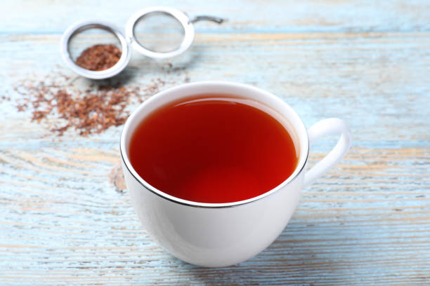 Freshly brewed rooibos tea and dry leaves on light wooden table