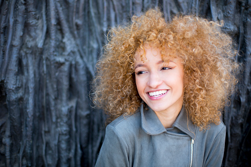 portrait young latin woman with curly afro hair smiling outdoors with soft light