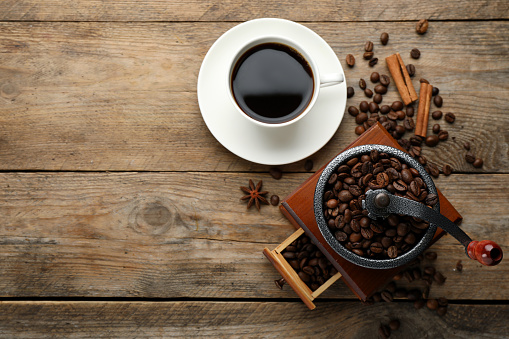 Vintage manual coffee grinder, beans and cup of drink on wooden table, flat lay. Space for text