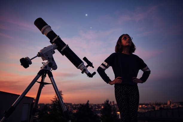 istock Girl with astronomical telescope stargazing under twilight sky. 1392922490