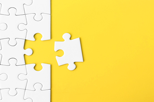 White jigsaw puzzle on yellow background with copy space. Concept for: business strategy, teamwork and problem solving