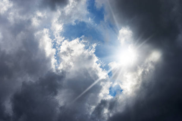 Close-up of a dark dramatic cloudy sky with sunbeams, backlit, full frame, photography.