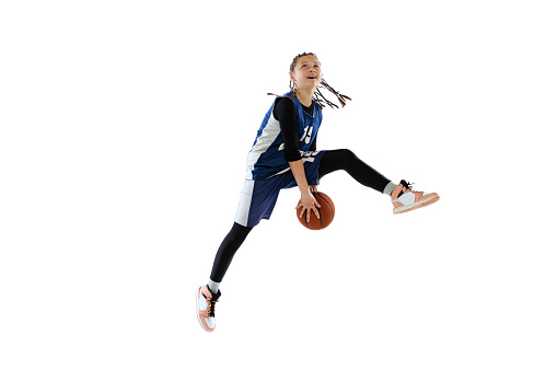 Dynamic portrait of teen girl, basketball player training, jumping with ball isolated over white studio background. Bounce pass . Concept of professional sport, active lifestyle, hobby, team game