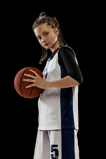 Portrait of teen girl, motivated basketball player in uniform posing isolated over white studio background. Little champion. Concept of professional sport, childhood, motion, team game, success, ad