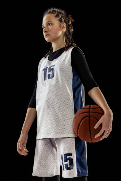 10代の女の子の肖像画、黒いスタジオの背景の上に孤立したポーズをとっている制服を着たバスケットボール選手。チームリーダー - basketball team sports healthy lifestyle isolated objects ストックフォトと画像