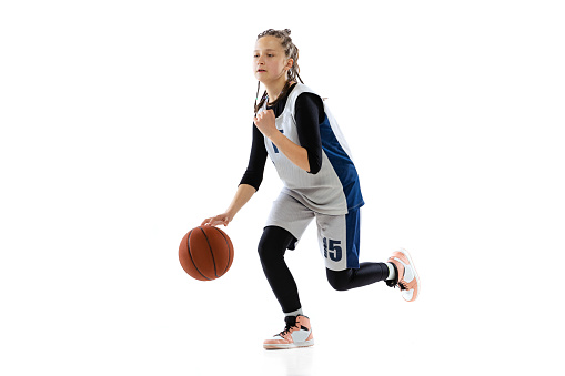 Studio shot of young girl, basketball player in blue uniform training isolated over white background. Dribbling ball before throwing. Concept of sport, active lifestyle, health, team game and ad