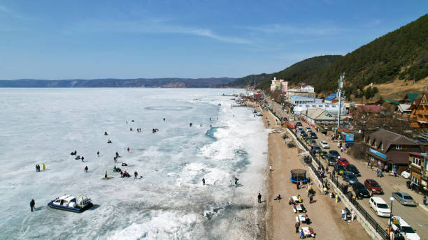 baikalsee im zeitigen frühjahr. touristen laufen auf dem eis, ein luftkissenfahrzeug befördert passagiere. dorf listwjanka, ein beliebter ort zum reisen - baikalsee stock-fotos und bilder