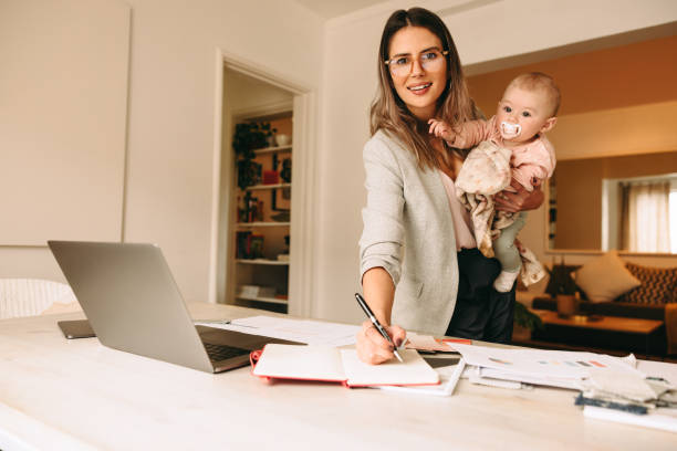 istock Creative businesswoman writing notes while holding her baby 1392938687