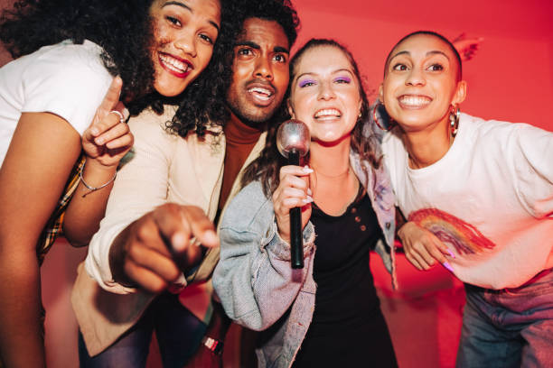 Happy friends singing into a mic on karaoke night stock photo