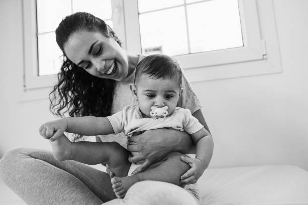 Young mother having fun with her son in bed at home - Focus on child face - Black and white editing stock photo