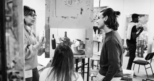 Photo of Mature teacher working with art students during painting class at school - Focus on boy face - Black and white edition