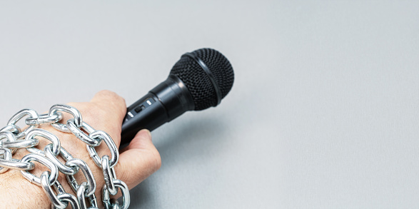 Male hand holding microphone tied with chains on grey background with copy space. Banner with place for text.