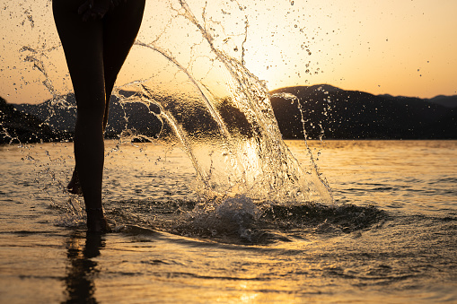 Rear-view of unrecognizable woman, splashing the water at the sea, during amazing sunset.