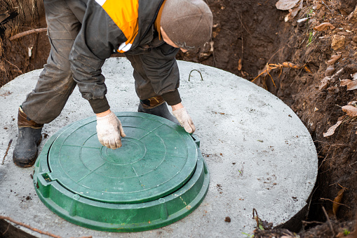 a utility worker lifts a manhole cover for sewerage maintenance and pumping out feces. Septic on a residential lot