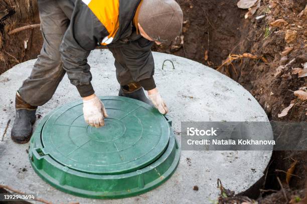 A Utility Worker Lifts A Manhole Cover For Sewerage Maintenance And Pumping Out Feces Septic On A Residential Lot Stock Photo - Download Image Now