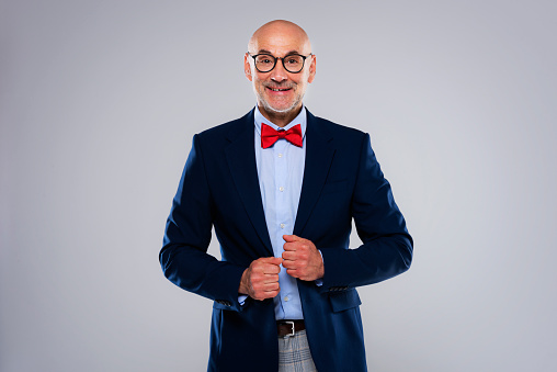 Cropped shot of smiling businessman wearing suit and bow tie while standing at isolated grey background. Copy space.