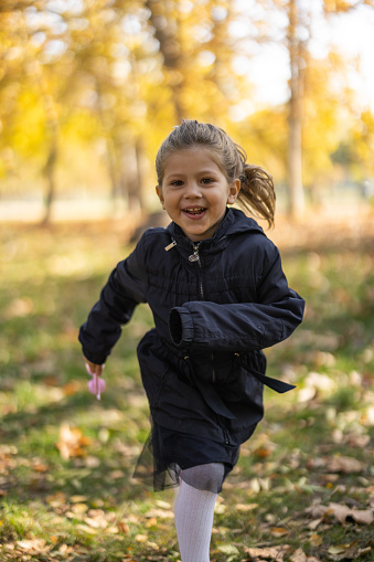 Front view of smiling little girl happily running in nature on sunny autumn day
