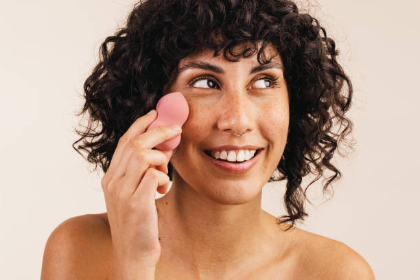 Pretty woman using a beauty blender on her face Pretty young woman looking away with a smile while using a makeup sponge on her face. Happy young woman using a beauty blender to apply makeup foundation on her face. foundation make up stock pictures, royalty-free photos & images