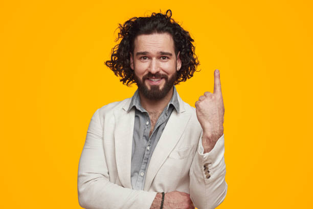 istock Smiling young unshaven man pointing up in yellow studio 1392954890
