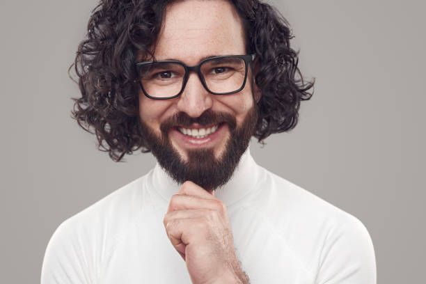 istock Confident young man smiling and touching chin in gray studio 1392954944