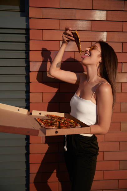 Cheerful woman eating pizza in city stock photo