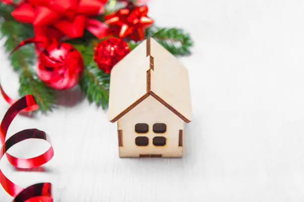 Photo of Wooden miniature house on white background and layout of Christmas tree, balls, gifts. Close up and copy space, selective focus.