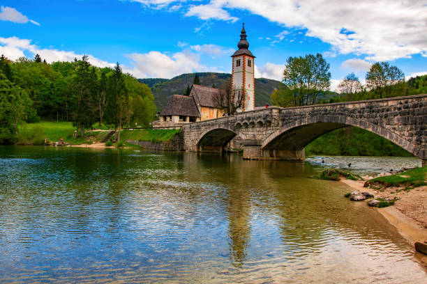 vista panoramica del ponte di pietra e della chiesa di san giovanni battista sul lago di bohinj, slovenia - shingle bank foto e immagini stock