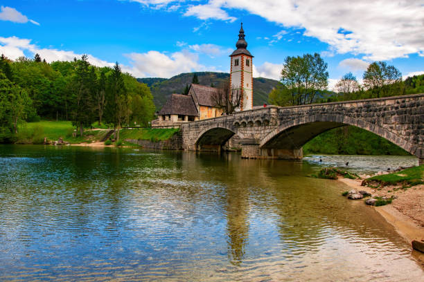 scenic view of stone bridge and church of st john the baptist on bohinj lake, slovenia - shingle bank imagens e fotografias de stock