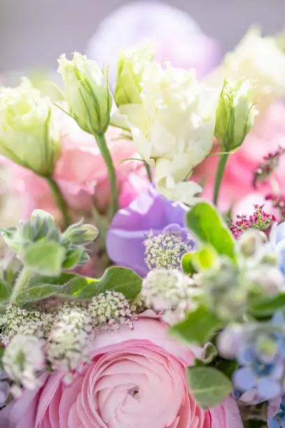 Close-up of a flower bouquet spring time wedding, dreamy style with shallow depth of field. The boquet contains pink ranunculus, white roses and other flowers. Vertical shot with copy space.