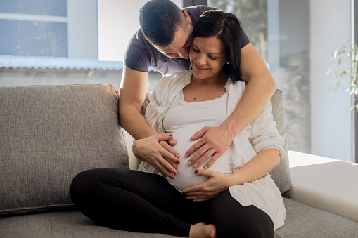 Man touching belly of his pregnant wife on sofa at home