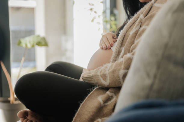istock Pregnant woman touching her belly on sofa 1392978143