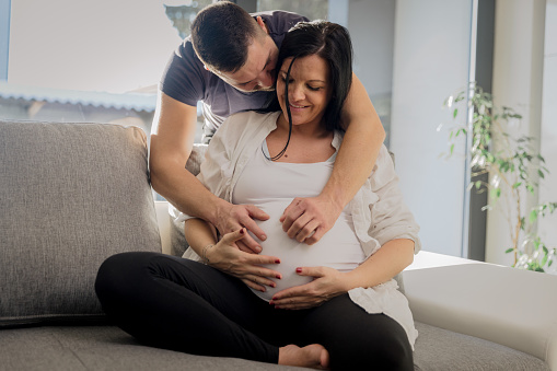 Man embracing his pregnant wife from behind and touching belly at home